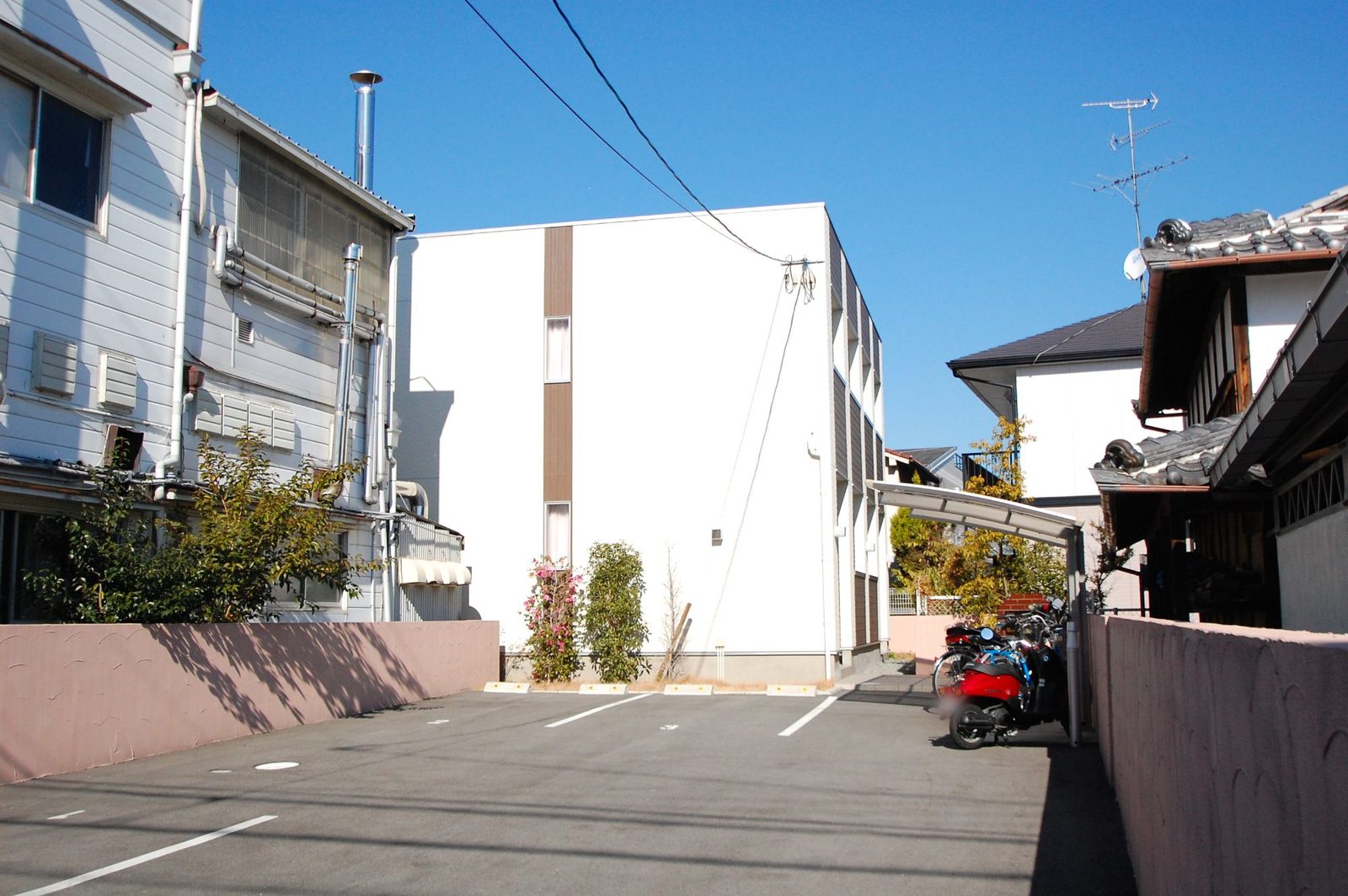 白い外壁に茶色のアクセントが入った2階建てアパートと、手前の駐車場