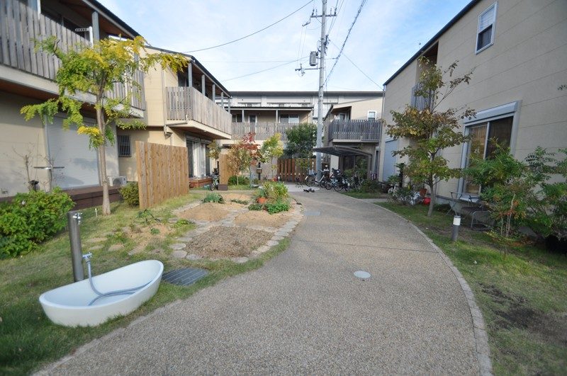 住宅に囲まれた芝生と植栽の緑地、中央を通る小道